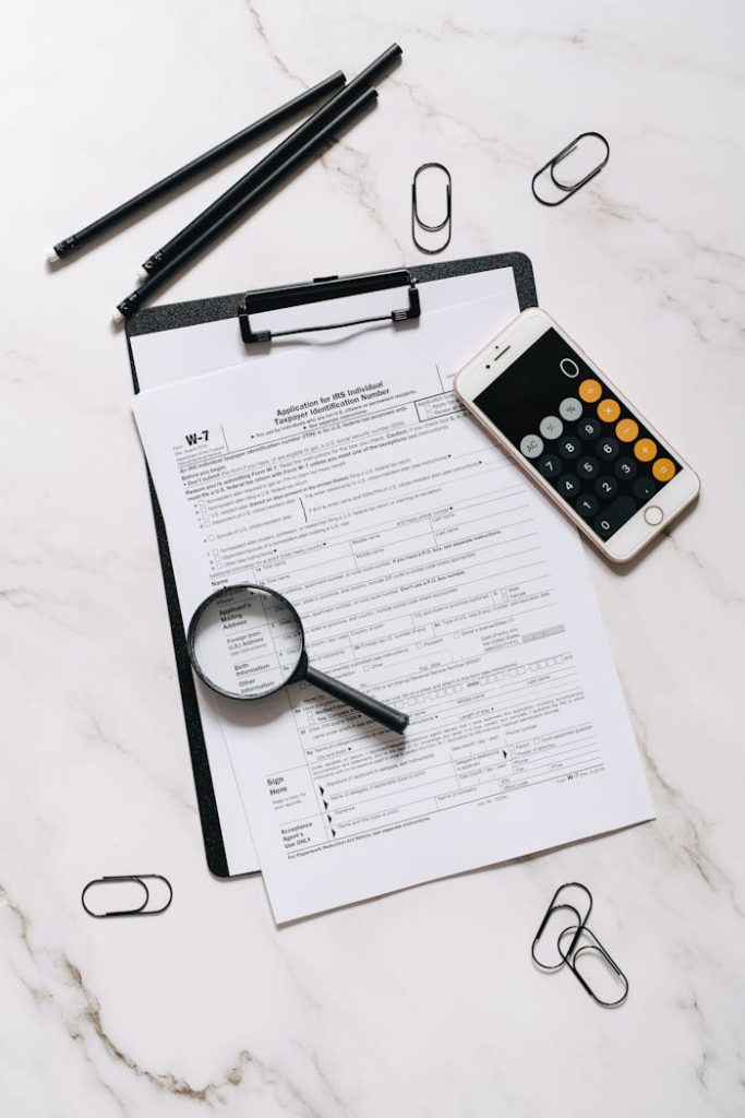 High angle shot of tax form, magnifying glass, and smartphone calculator on marble surface.
